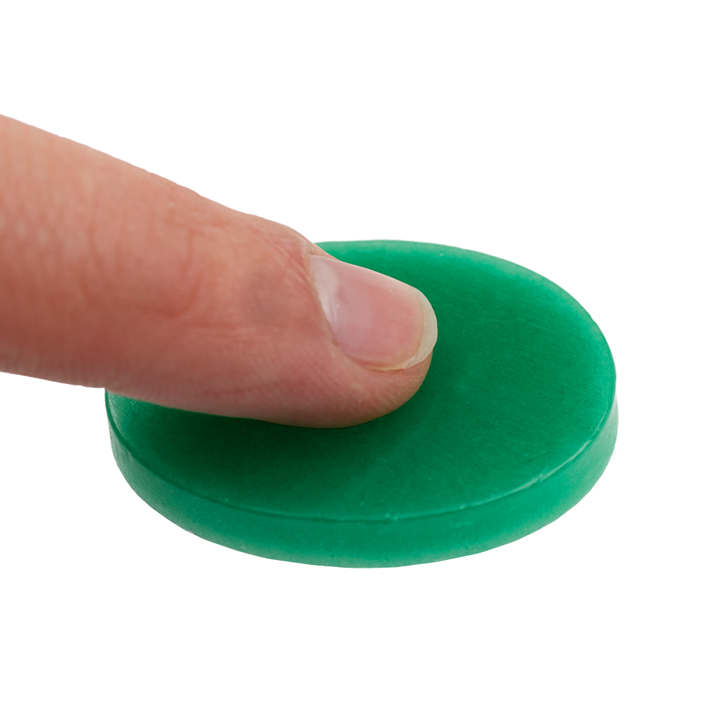 604_Fingerwachs_2 Auf dem Bild sieht man einen Finger, der auf eine grüne Scheibe Fingerwachs drückt. Das Produkt wird zum Schutz und zur Pflege der Finger verwendet.