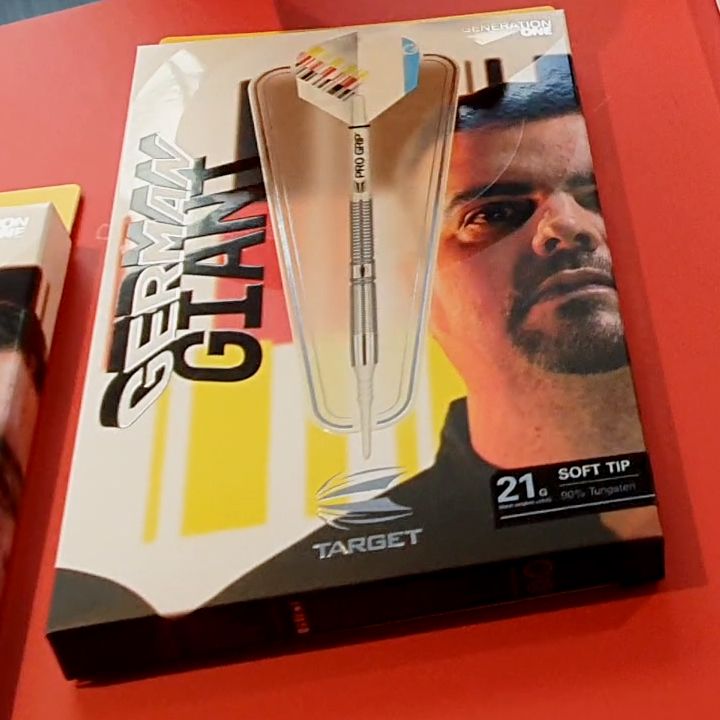GG-one Auf dem Bild sieht man eine Verpackung für Dartpfeile mit der Aufschrift "German Giant". Die Verpackung zeigt einen Dartpfeil und das Gesicht eines Mannes sowie die Angabe "21g Soft Tip".