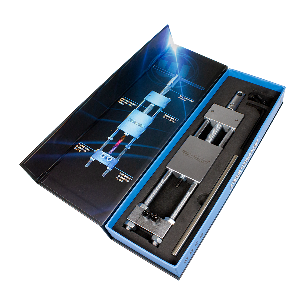 8425-Winmau-Craftsman-Re-pointing-System-5Rw3CTvWlDH1nL Das Bild zeigt das Produkt "Winmau Craftsman Re-Pointing System Spitzenwechsler" in einer geöffneten Verpackung. Das Werkzeug liegt ordentlich in einer Schaumstoffeinlage, daneben ist eine grafische Anleitung zu sehen.