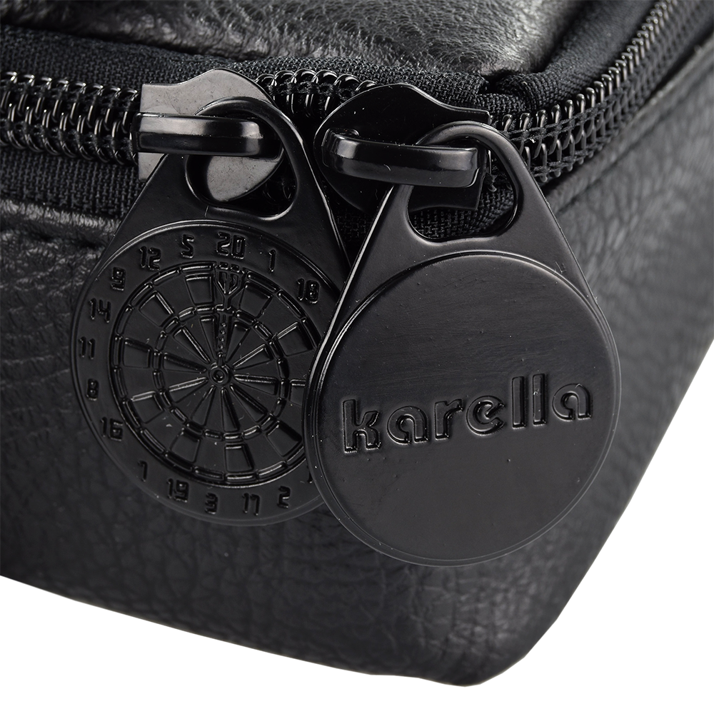 Pak5_Master_Pak_Leder_Edition_Darttasche_3 Das Bild zeigt einen Detailausschnitt der "Master Pak Leder Edition Darttasche". Zu sehen sind zwei schwarze Reißverschluss-Anhänger, einer davon mit einer Dartbord-Gravur und der andere mit dem Schriftzug "karella".