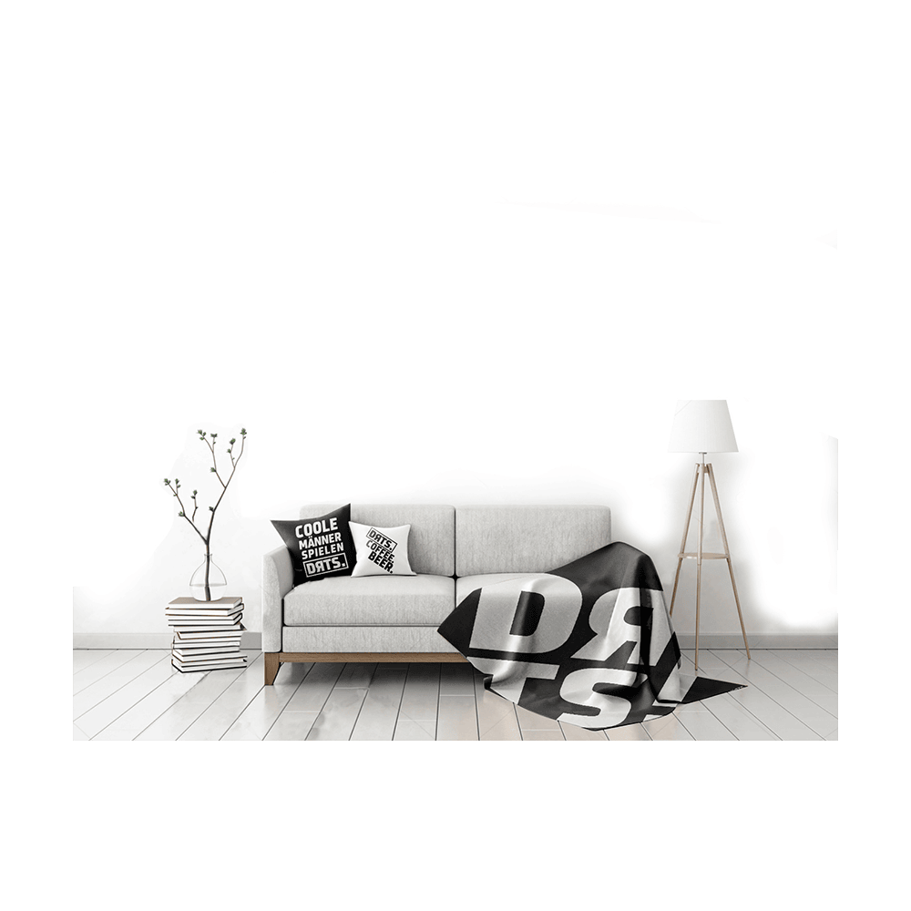 DRTS_K1_DRTS_Kissen_Schwarz_3 Das Bild zeigt ein modern eingerichtetes Wohnzimmer mit einem hellgrauen Sofa. Auf dem Sofa liegt das Produkt "SPORT1 DRTS. Kissen" mit auffälligem schwarzen und weißen Schriftzug.