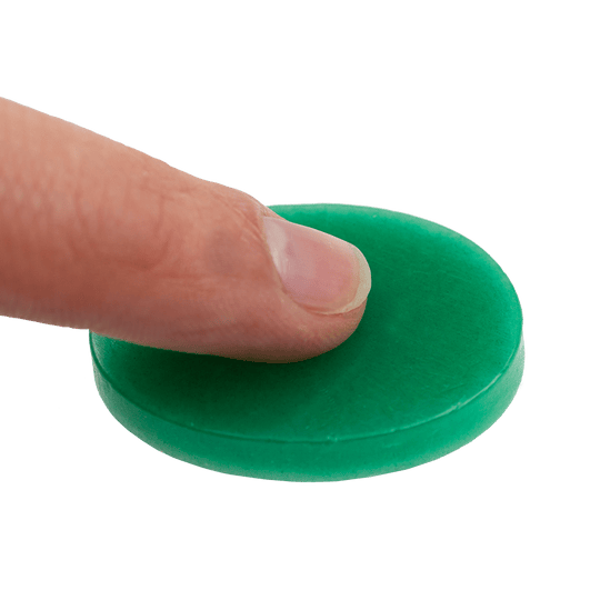 604_Fingerwachs_2 Auf dem Bild sieht man einen Finger, der auf eine grüne Scheibe Fingerwachs drückt. Das Produkt wird zum Schutz und zur Pflege der Finger verwendet.