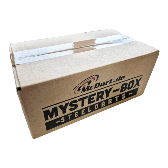 Auf dem Bild ist ein Karton mit der Aufschrift "McDart.de Mystery-Box - Steeldarts" zu sehen. Die Box ist oben mit Klebeband verschlossen.
