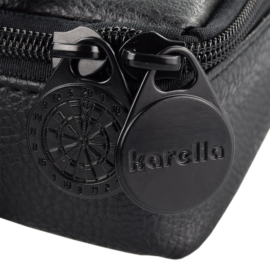 Pak5_Master_Pak_Leder_Edition_Darttasche_3 Das Bild zeigt einen Detailausschnitt der "Master Pak Leder Edition Darttasche". Zu sehen sind zwei schwarze Reißverschluss-Anhänger, einer davon mit einer Dartbord-Gravur und der andere mit dem Schriftzug "karella".