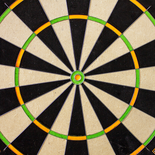 3023_Winmau_Champions_Choice_DualCore_Dartboard_31OalkqlJd5YsR Das Bild zeigt die Mitte eines Winmau Champions Choice DualCore Dartboards. Die Felder sind abwechselnd schwarz und weiß, mit grünen und orangefarbenen Ringen.